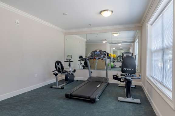 A spacious home gym with a treadmill, exercise bike, and mirror. at Snowden Senior Apartments, Virginia, 23605