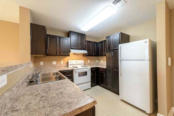 A kitchen with a white refrigerator and brown cabinets. at The Grande at Granite Falls LLC Apartments, North Carolina, 27571