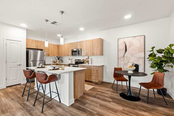A modern kitchen with a white island and brown chairs.