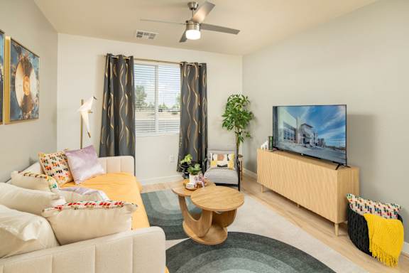 A living room with a white couch, a wooden coffee table, a flat screen TV, and a ceiling fan.