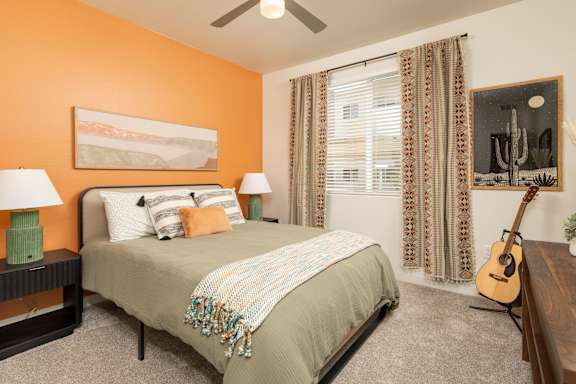 A bedroom with a bed, two lamps, a guitar, and a painting on the wall.