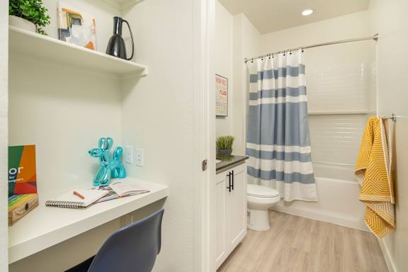 A small bathroom with a white desk and a blue chair.