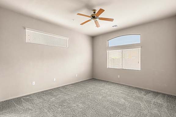 A room with a ceiling fan and two windows.