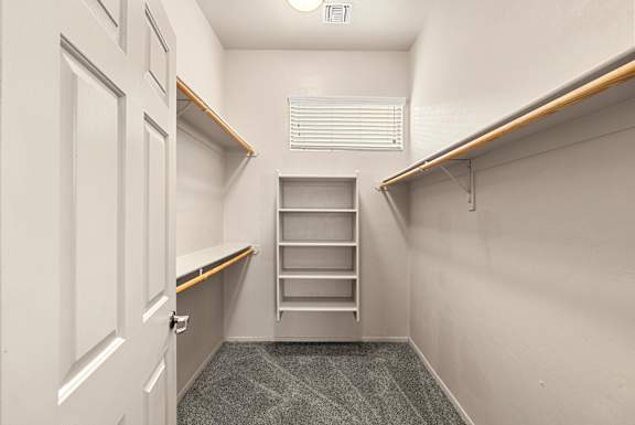 A white door is on the left of a hallway with a shelf and a vent on the wall.