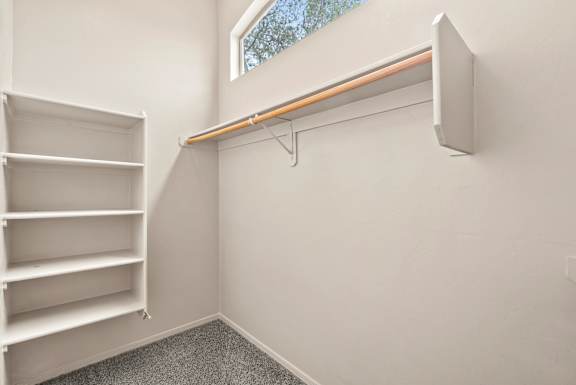 A white shelving unit sits in a corner of a room with a window.