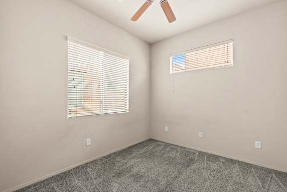 A room with a ceiling fan and two windows with blinds.