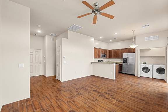 A room with a ceiling fan and a kitchen area with a refrigerator and washing machine.