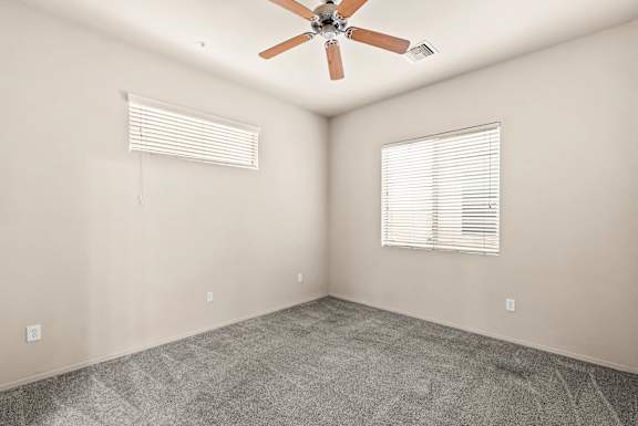 A room with a ceiling fan and two windows with blinds.