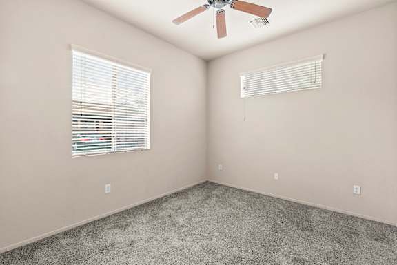A room with a ceiling fan and two windows with blinds.