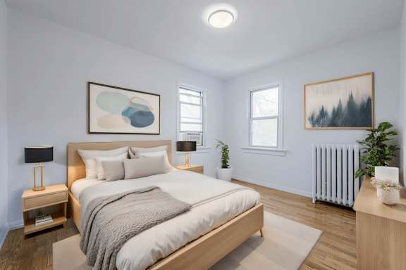 A bedroom with a large bed, a nightstand with a lamp, and a plant on the side table.