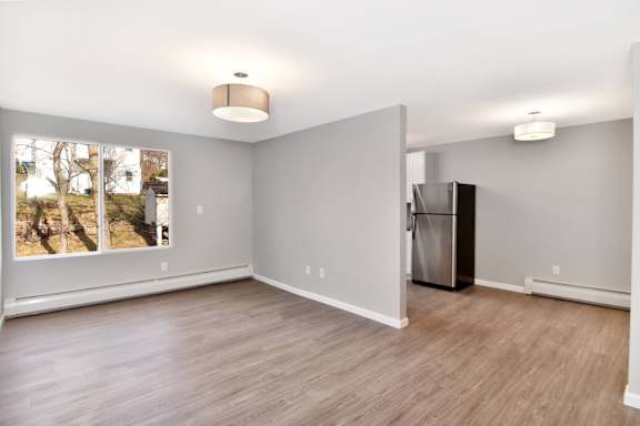 an empty living room with a large window and a refrigerator