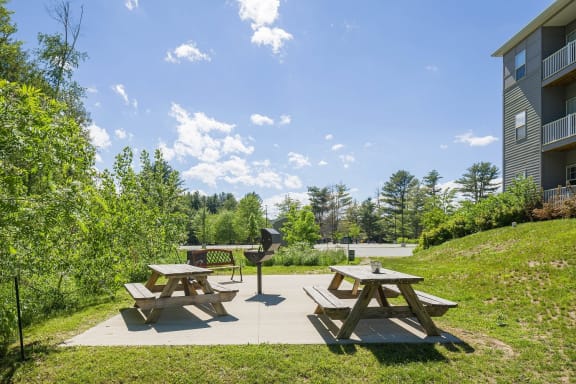 two picnic tables and a grill on a patio in front of a building
