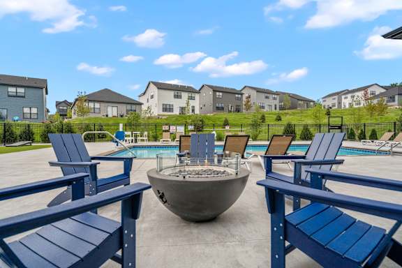 A poolside area with blue chairs and a fire pit.