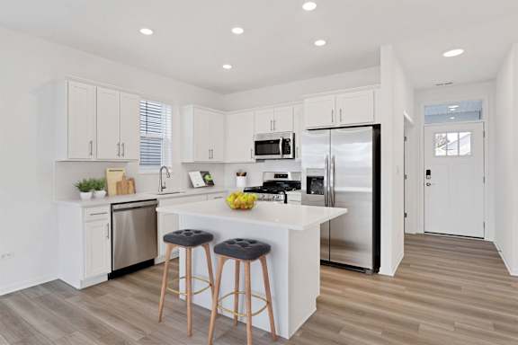 A kitchen with white cabinets and a white island with a bowl of fruit on it.