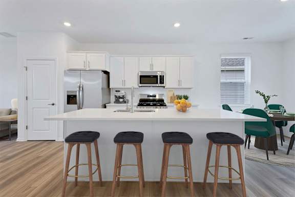 A kitchen with white cabinets and a white island with bar stools.
