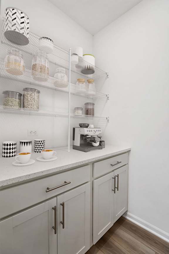 A kitchen with white cabinets and a white countertop with a coffee maker and two cups on it.