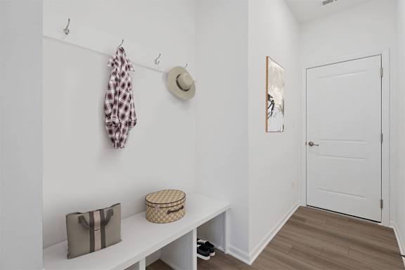 A hallway with a coat rack, a hat, a bag, and a basket on a bench.