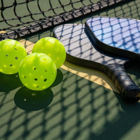 three pickle balls and 2 rackets on a court