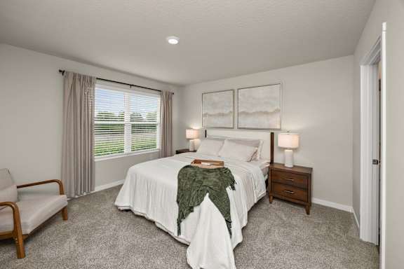 A bedroom with a bed, nightstand, chair, and window.