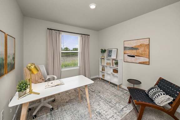 A room with a white desk, a chair, a couch, and a painting on the wall.