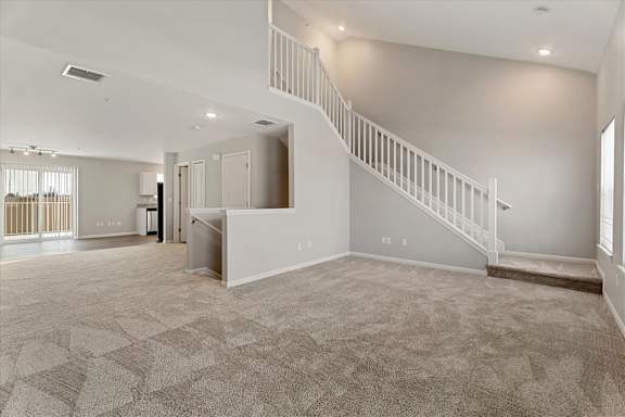 A spacious living room with a staircase and a kitchen area in the background.