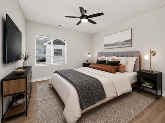 A bedroom with a large bed, a ceiling fan, and a window with blinds.