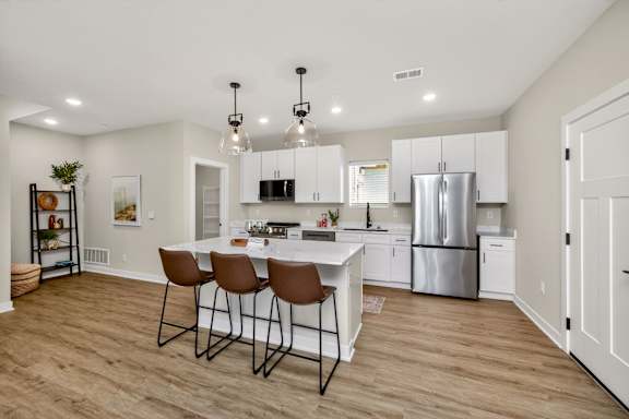 A kitchen with white cabinets and a center island with chairs.