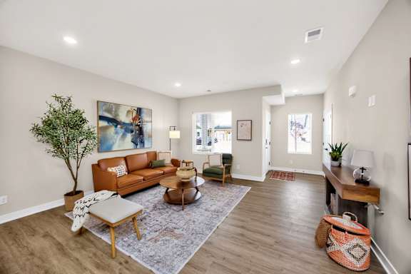 A living room with a brown sofa, a tree, and a painting on the wall.