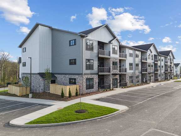 A row of modern townhouses with a parking lot in front.