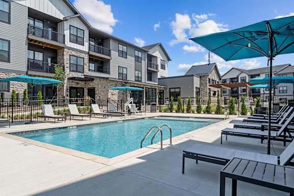 A swimming pool surrounded by lounge chairs and umbrellas in front of apartment buildings.