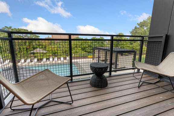 a balcony with two chairs and a table and a pool in the background