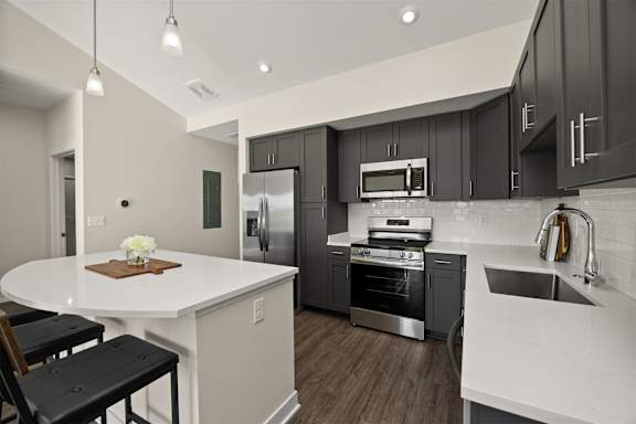 A modern kitchen with a white island and black stools.