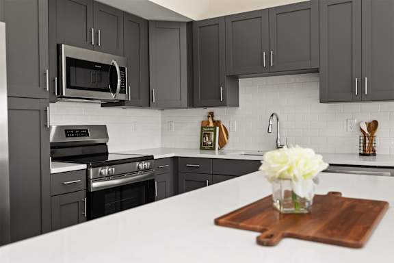 A kitchen with a white counter top and a wooden cutting board with a white flower on it.