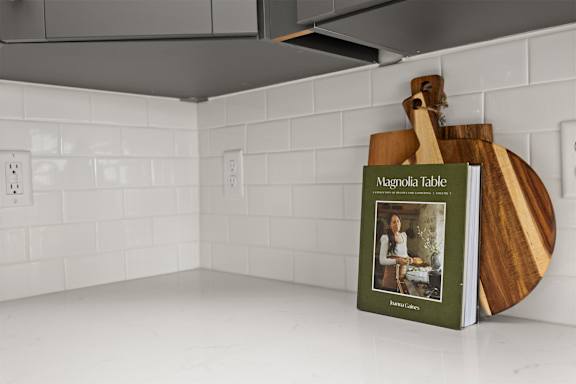 A Magnolia Table book is on a wooden cutting board in a kitchen.