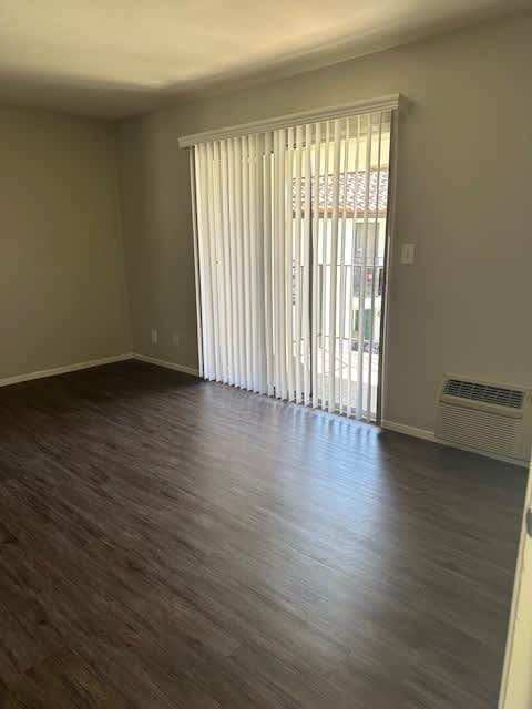 A room with a window covered by white blinds and a wood floor.