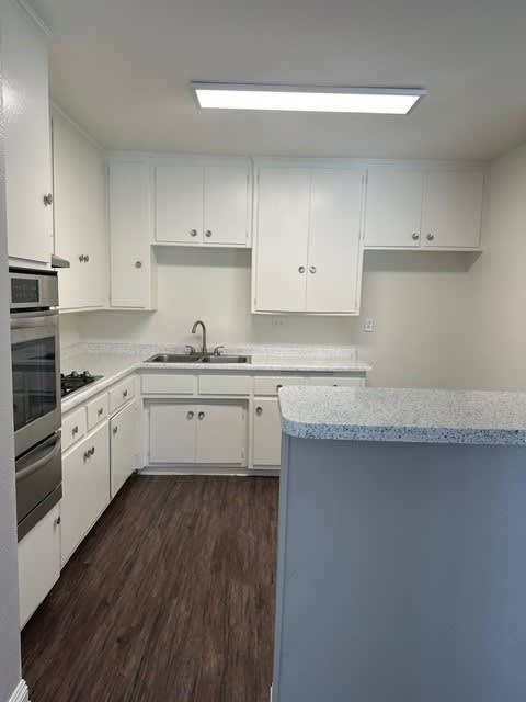 A kitchen with white cabinets and a wooden floor.