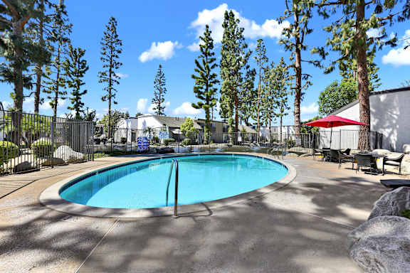 A swimming pool surrounded by trees and a fence at THE STREAMS Apartments, Fullerton