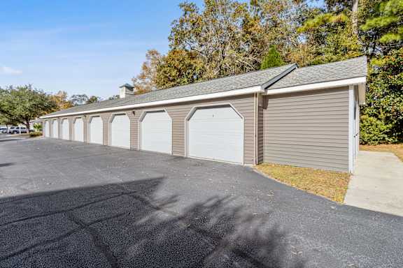 A long building with a grey roof and a parking lot in front.