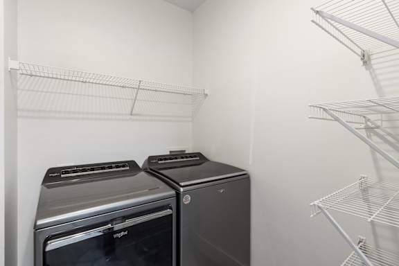 Two black ovens are in a white room with empty shelves.