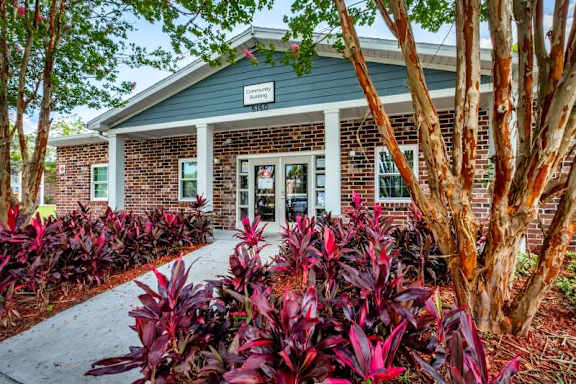 A building with a green roof and a sign that says "Community Center" is surrounded by red plants and trees.