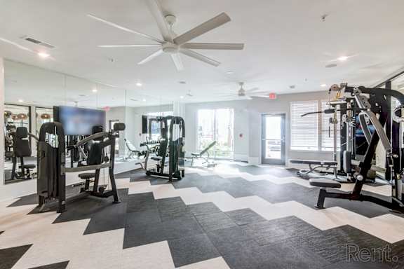 A spacious gym with a variety of equipment and a ceiling fan at Tapestry Nona Apartments in Orlando, FL
