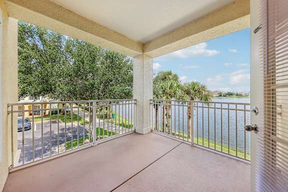 A balcony with a metal railing and a view of a parking lot and trees.