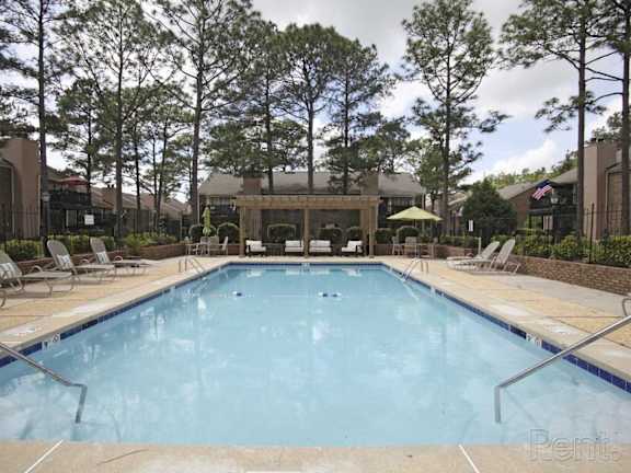 A large swimming pool surrounded by trees and lounge chairs The Oakley at Hillcrest in Mobile, AL