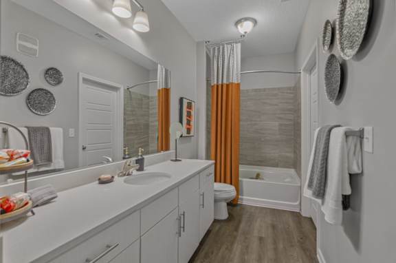 A bathroom with a white countertop and orange curtains.