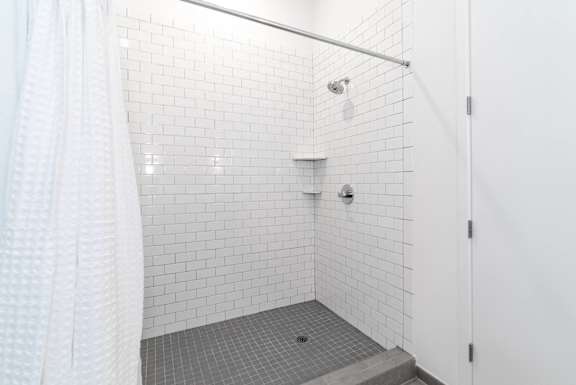 a white tiled shower in a bathroom with a shower curtain at 20 Midtown, Birmingham, 35233