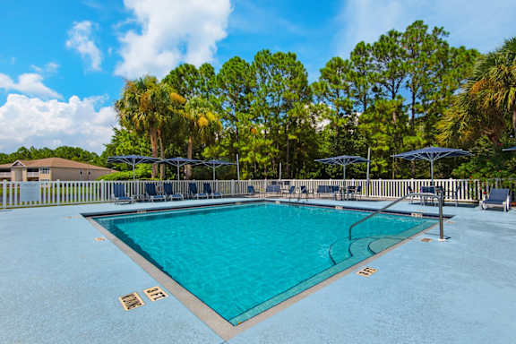 An outdoor swimming pool surrounded by trees and umbrellas at Crystal Lake in Pensacola, Florida.