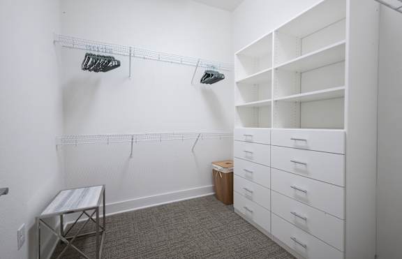 a walk in closet in a room with white walls and shelves and a white bench at 20 Midtown, Birmingham, Alabama
