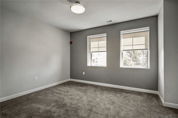 an empty living room with two windows and gray walls