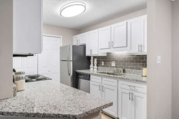 A kitchen with granite countertops, white cabinets, and a laundry closet at Summerchase at Riverchase in Hoover, Alabama.