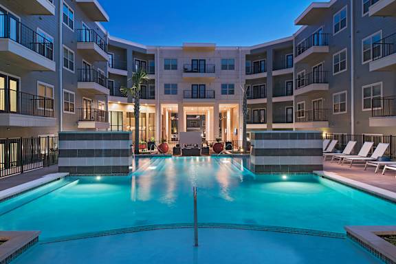 A large swimming pool in front of a building with a balcony.